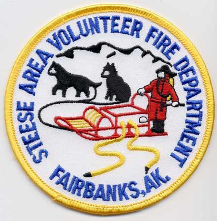 Fairbanks - Distintivo bianco con al centro un pompiere su slitta