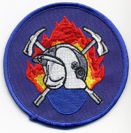 Ledegem - Distintivo blu con al centro un elmo su sfondo di fiamme