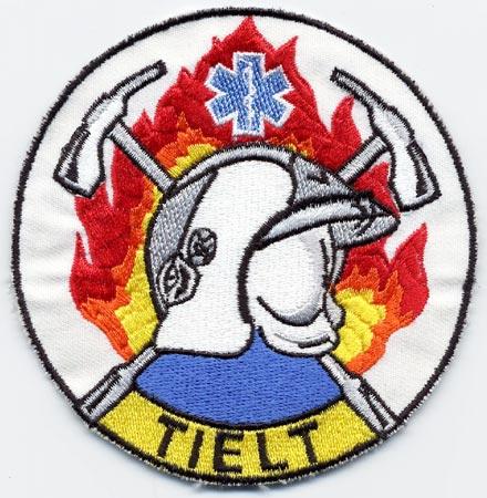 Tielt - Distintivo bianco con al centro un elmo su sfondo di fiamme