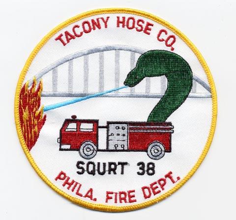 Tacony - Distintivo bianco con al centro un mezzo antincendio e fiamme