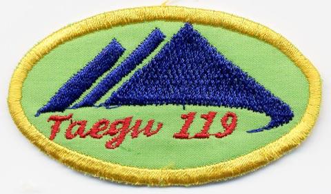 Taegu - Distintivo verde con al centro montagne blu